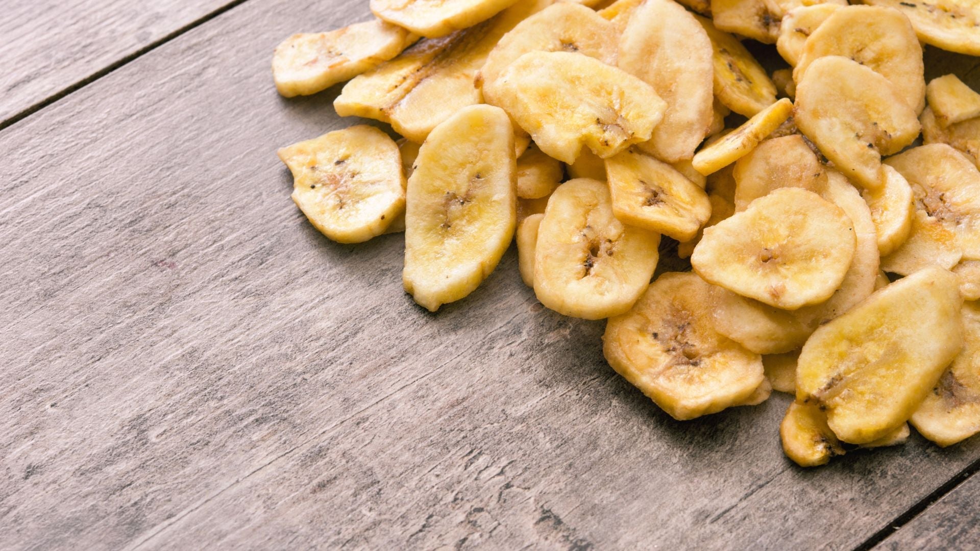 Pile of dried banana slices on a wooden table, showcasing yellow, crispy tropical fruit snacks.